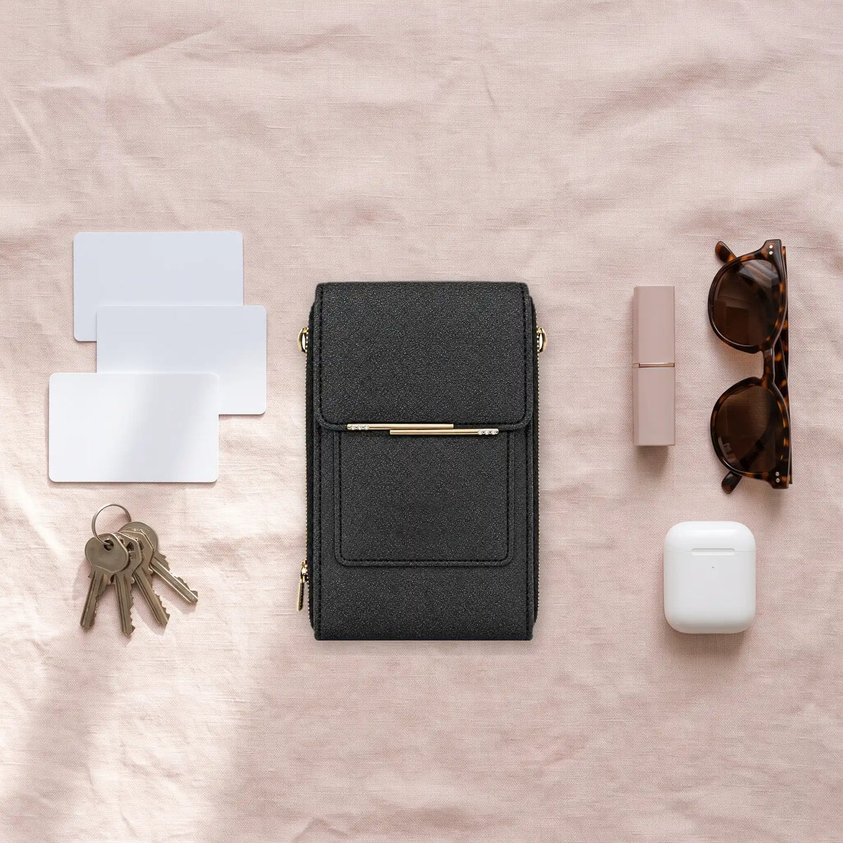 Bolso negro rodeado de lo que cabe: tarjetas, llaves, labial, gafas y estuche de audífonos
