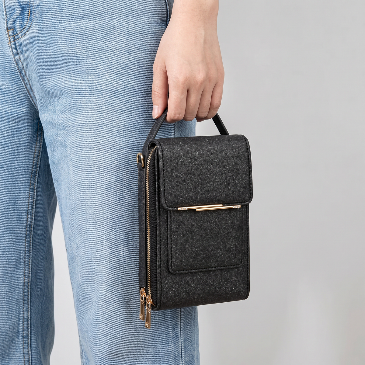 Bolso negro sostenido en la mano junto al jean para ver su tamaño compacto